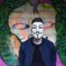 man in white mask in black crew neck shirt and blue zip up jacket infront graffiti wall