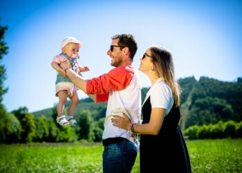 man in white and red polo shirt carrying girl in blue denim jeans during daytime
