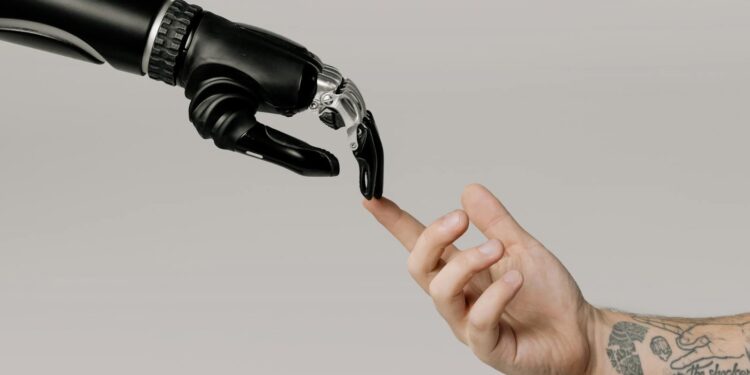 A human hand with tattoos reaching out to a robotic hand on a white background.